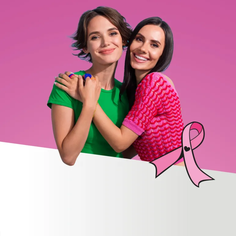 dwie uśmiechnięte, przytulone kobiety i różowa wstążka Różowego Października